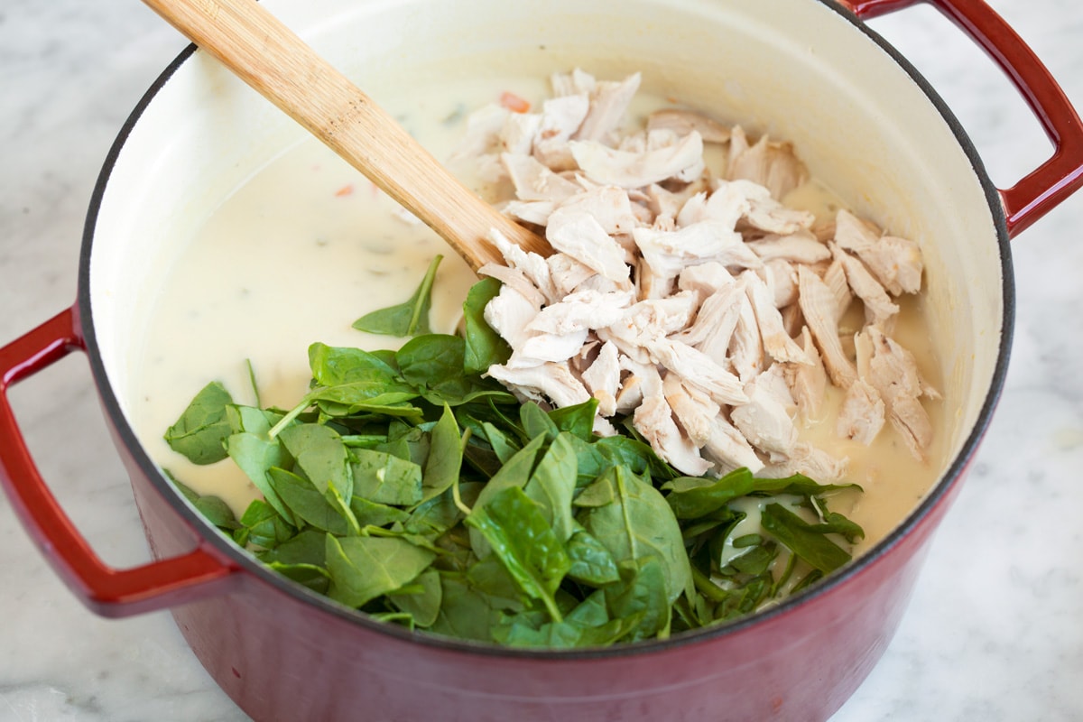 Adding cooked shredded chicken and spinach to pot.