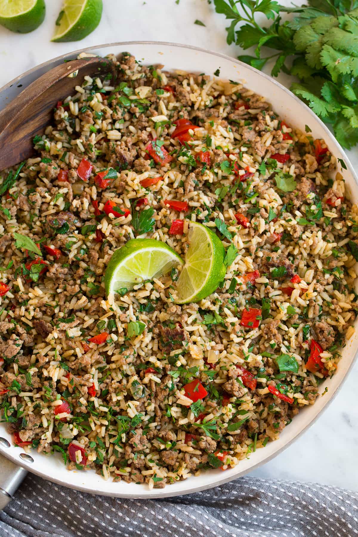 Overhead image of Chimichurri Beef and Rice in white skillet after completed. It's garnished with lime wedges.