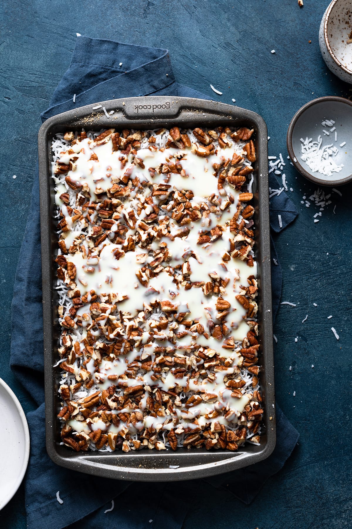 Showing how to make magic bars pouring sweetened condensed milk over chocolate chip layer in baking dish. 