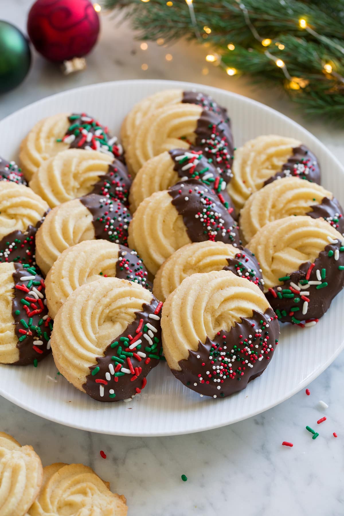 Butter Cookies dipped in chocolate and covered in sprinkles. Shown in rows on a white serving plate.