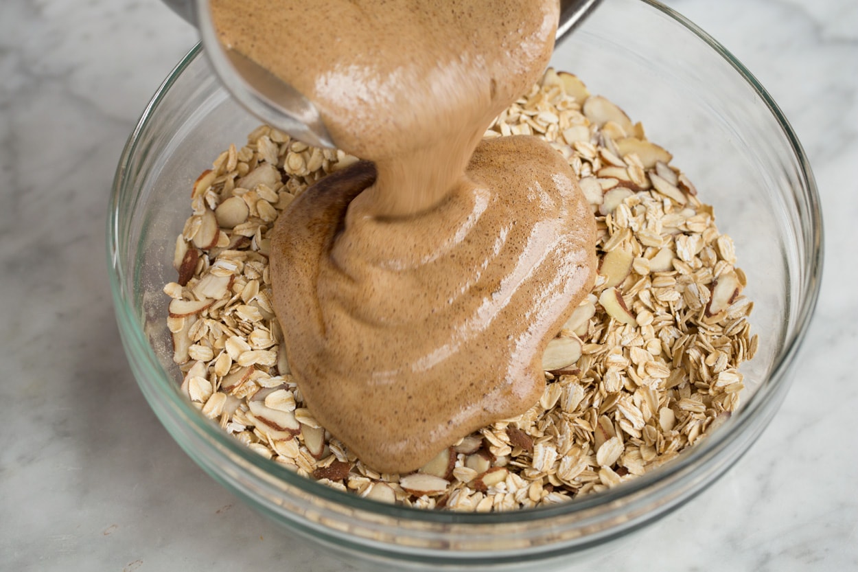 Pouring honey coating over oats in mixing bowl to make granola.