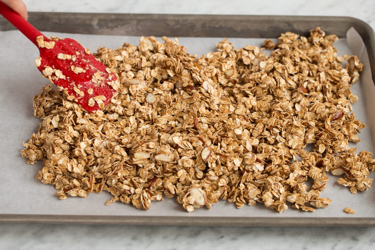Spreading granola mixture on parchment paper lined baking sheet to bake.