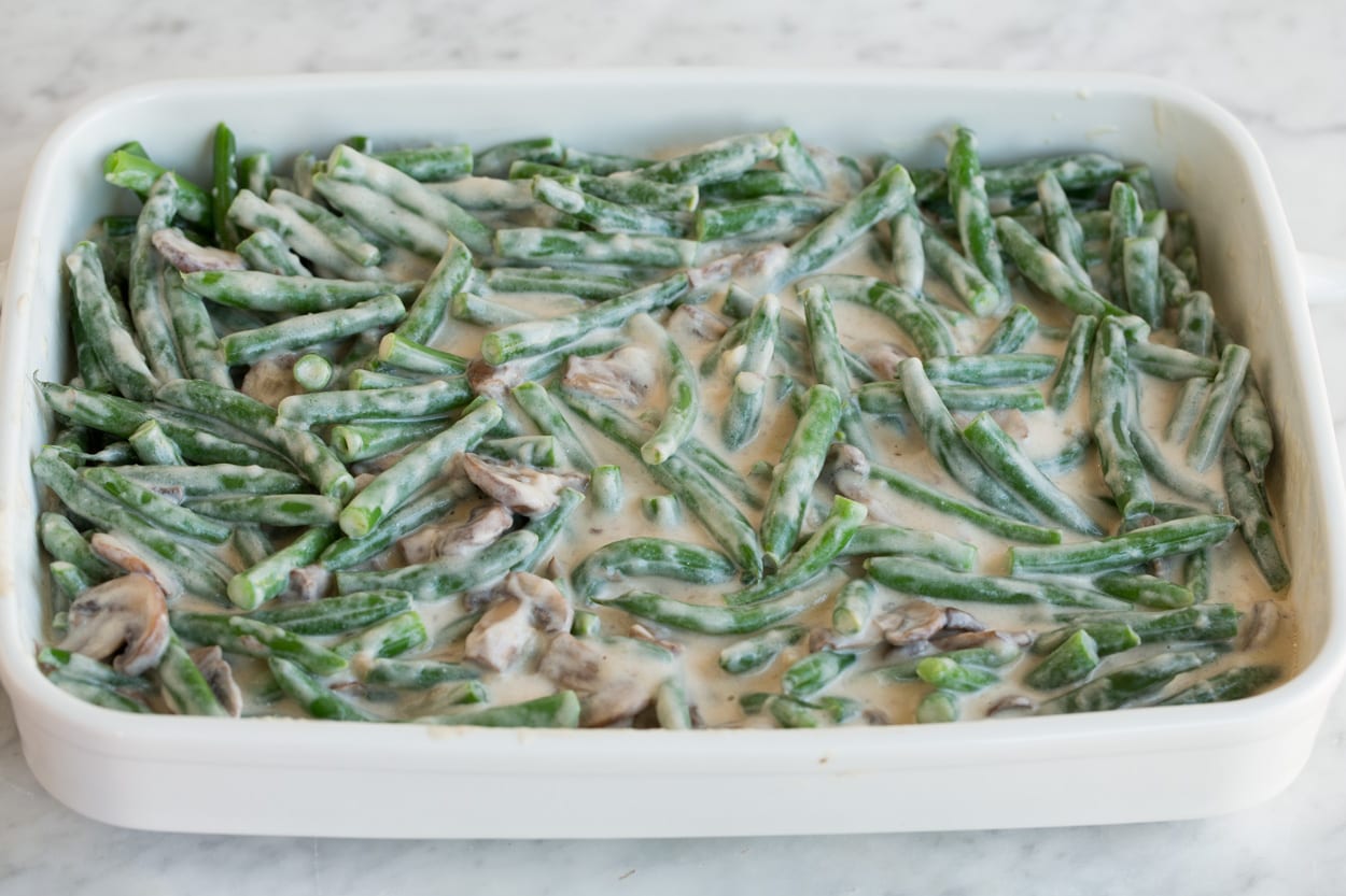 Creamy coated green beans and mushrooms in a white ceramic baking dish before baking, for Green Bean Casserole.