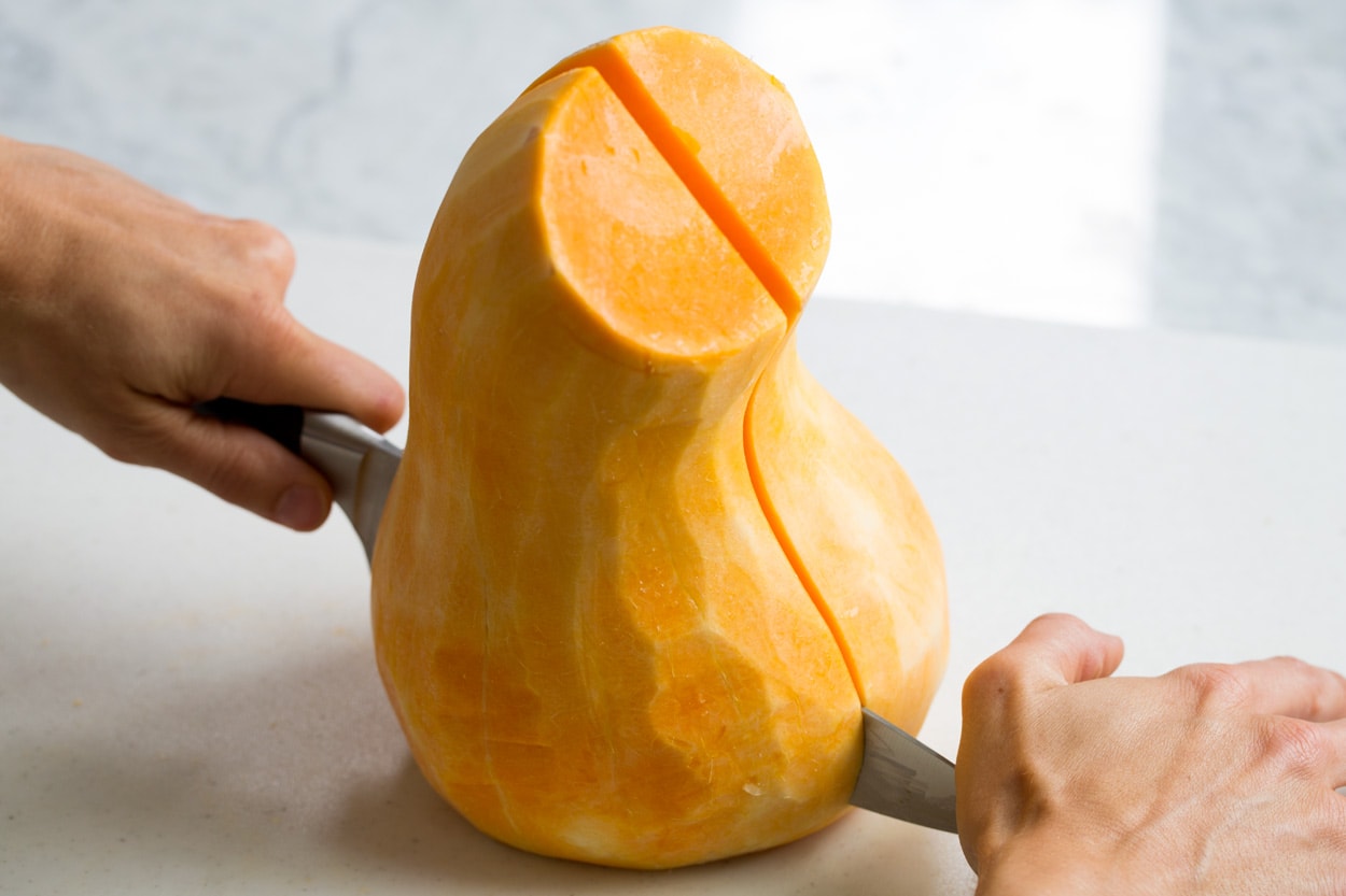 Showing how to halve a butternut squash on a cutting board.