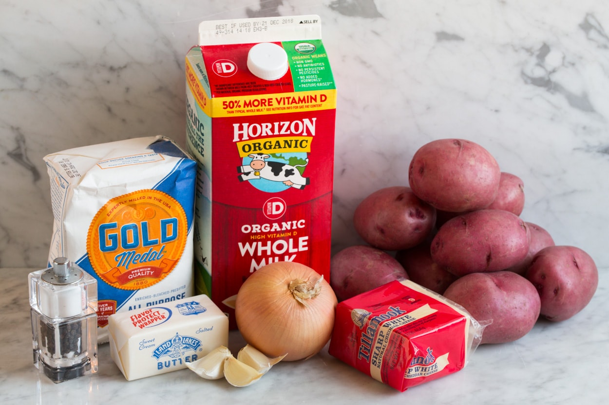 Ingredients for scalloped potatoes shown here including whole milk, butter, flour, onion, garlic, red potatoes, sharp white cheddar cheese, salt and pepper.
