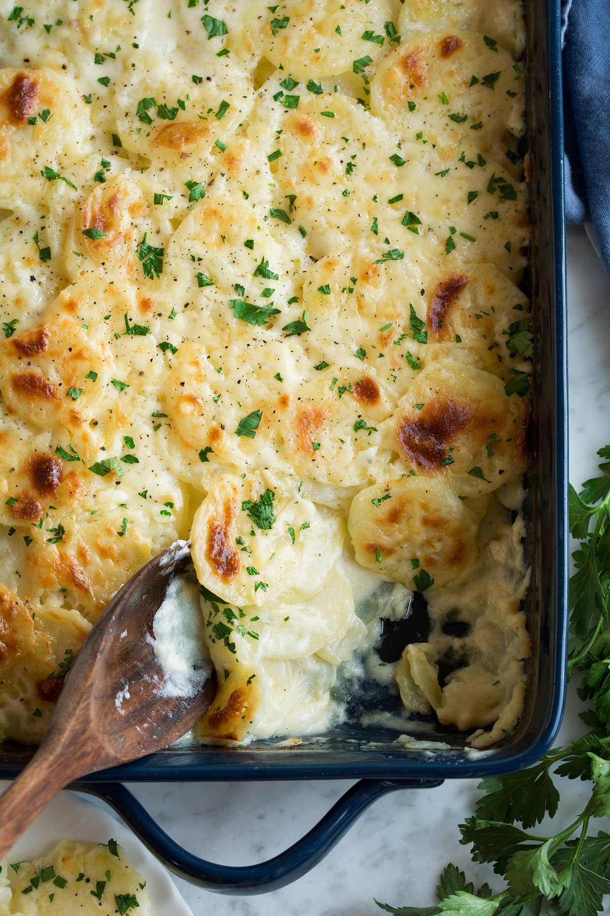 Scalloped Potatoes in a navy baking dish with one scoop removed to show creamy sauce and potato layers.