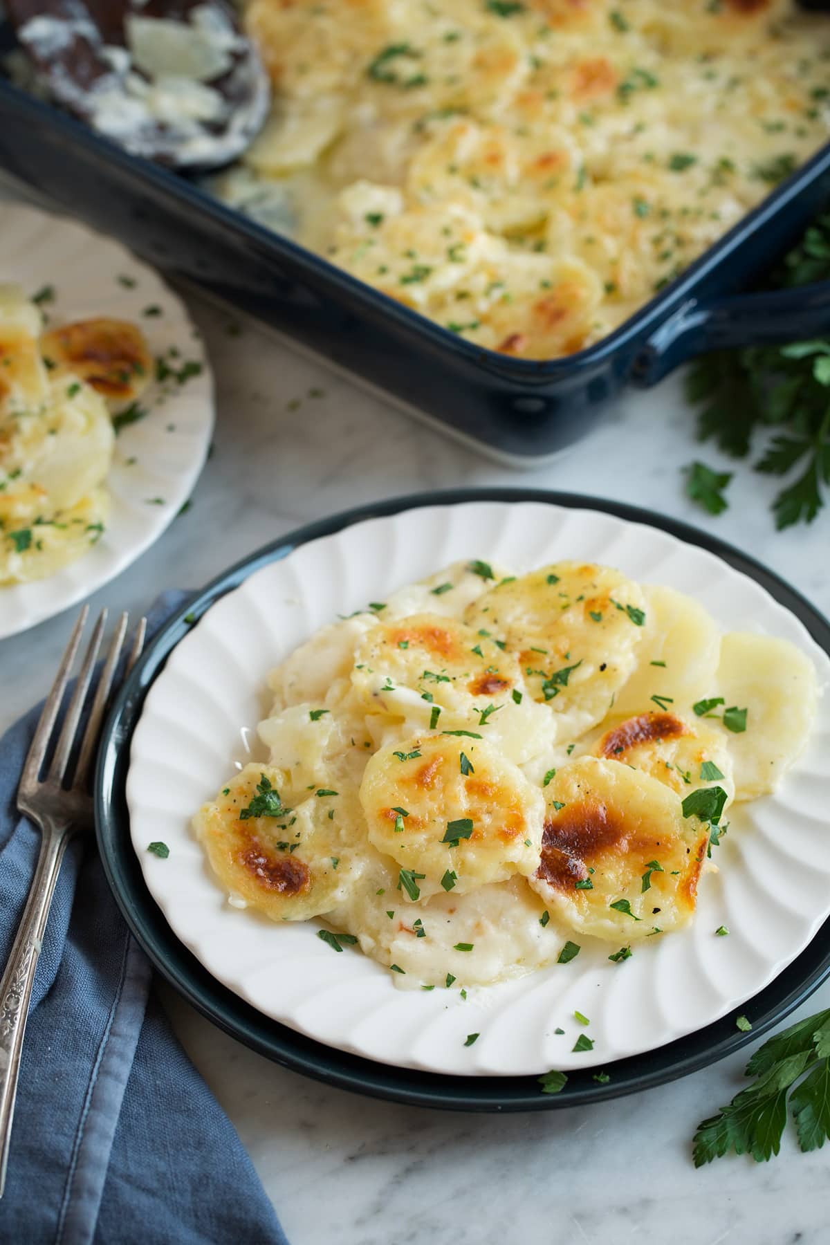 Scalloped Potatoes on a white single serving dish set over a dark blue plate that's resting on a marble surface.