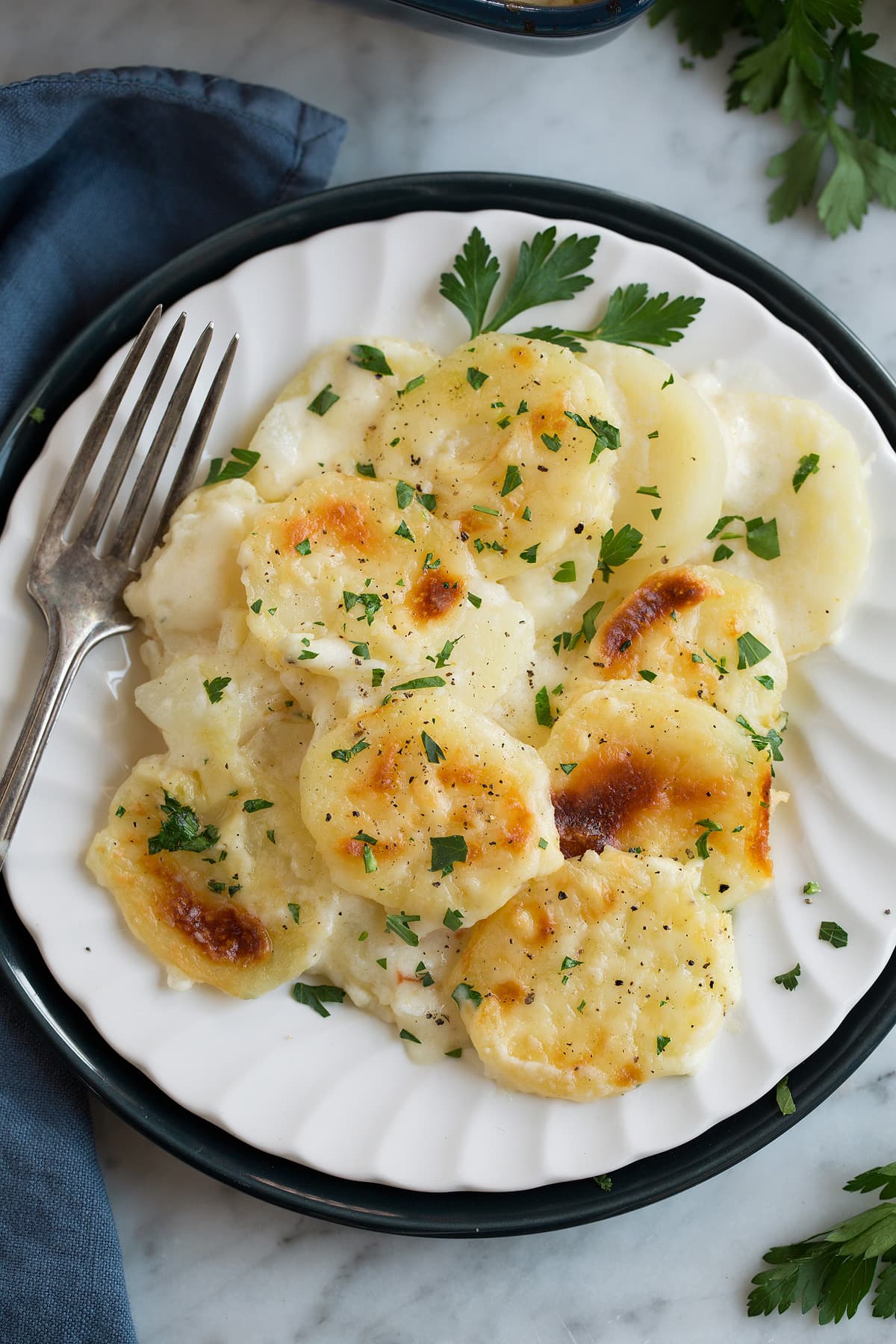 Scalloped Potatoes on a white single serving dish set over a dark blue plate that's resting on a marble surface.