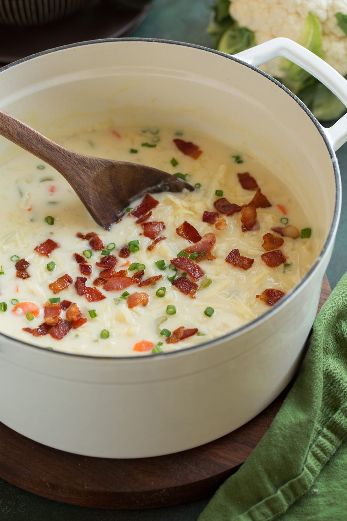 Pot full of cauliflower soup garnished with cheddar, bacon and green onions.