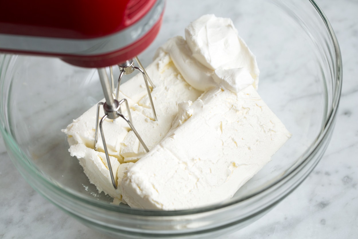 Showing how to make a cheeseball. Mixing cream cheese sour cream and seasoning in a mixing bowl with an electric hand mixer.