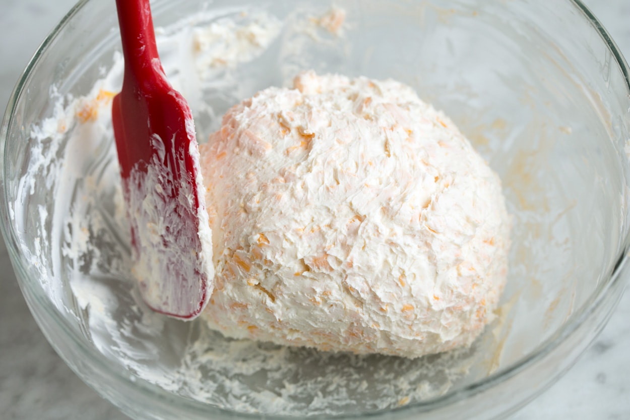 Forming chilled cheese ball mixture in bowl into a ball with a spatula.