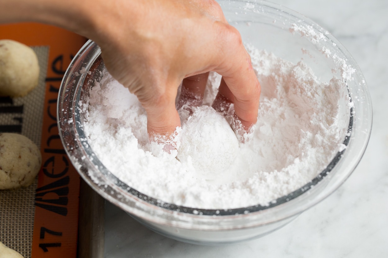 Rolling baked Mexican wedding cookies in powdered sugar after baking.