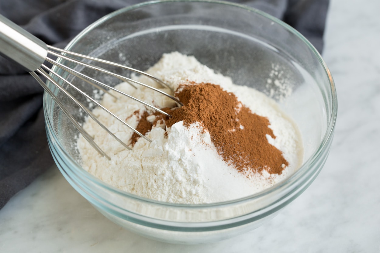 Showing how to make oatmeal raisin cookies. Whisking flour, cinnamon, baking soda, baking powder and salt in a glass mixing bowl.