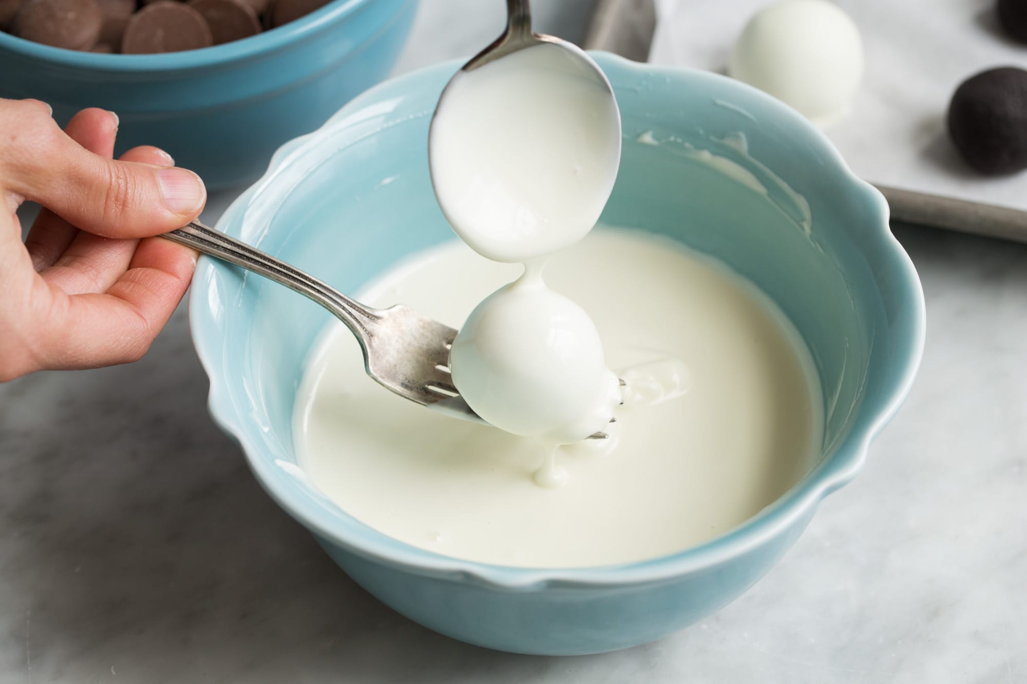 Dipping an oreo ball in melted white chocolate.