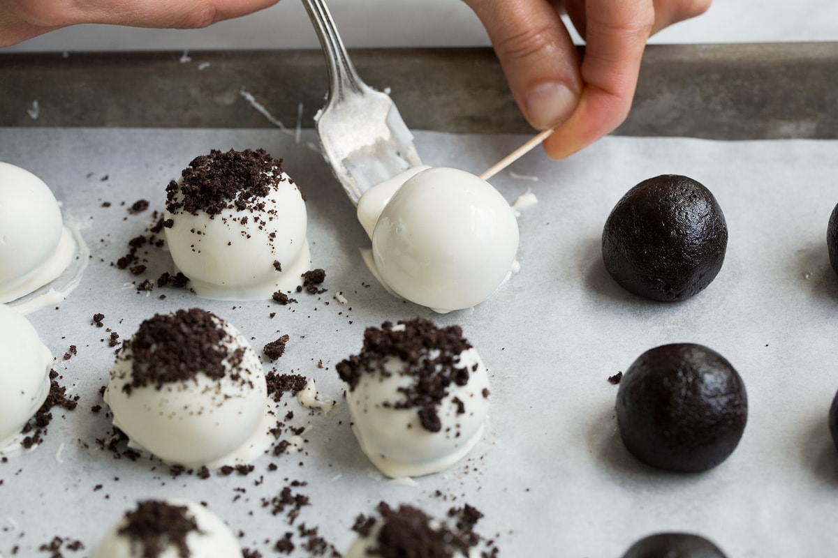 Transferring dipped oreo ball to parchment paper using a fork and toothpick.