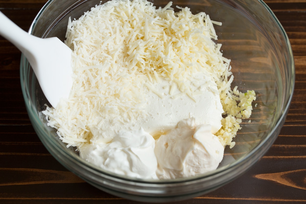 Mixing cream cheese, mayonnaise, sour cream, garlic and shredded cheeses in mixing bowl to make Spinach Artichoke Dip.