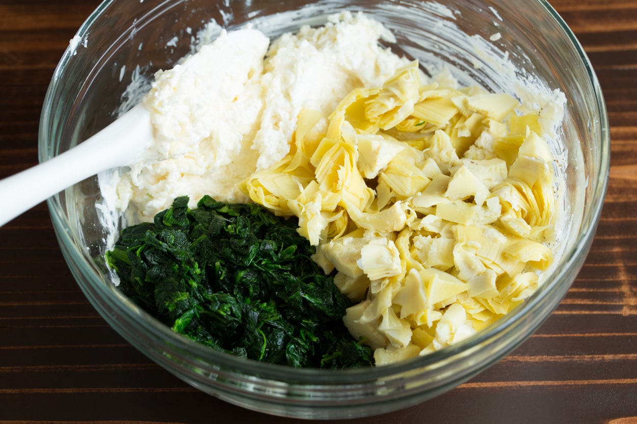 Mixing spinach and artichokes into Spinach Artichoke Dip mixture in mixing bowl.