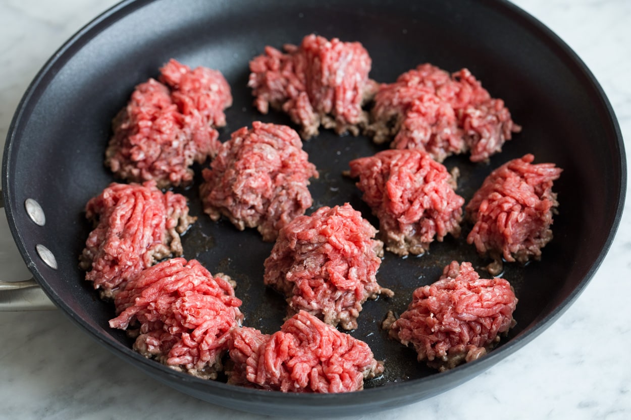 Showing how to make taco salad. Starting by browning chunks of ground beef in a large non-stick skillet.
