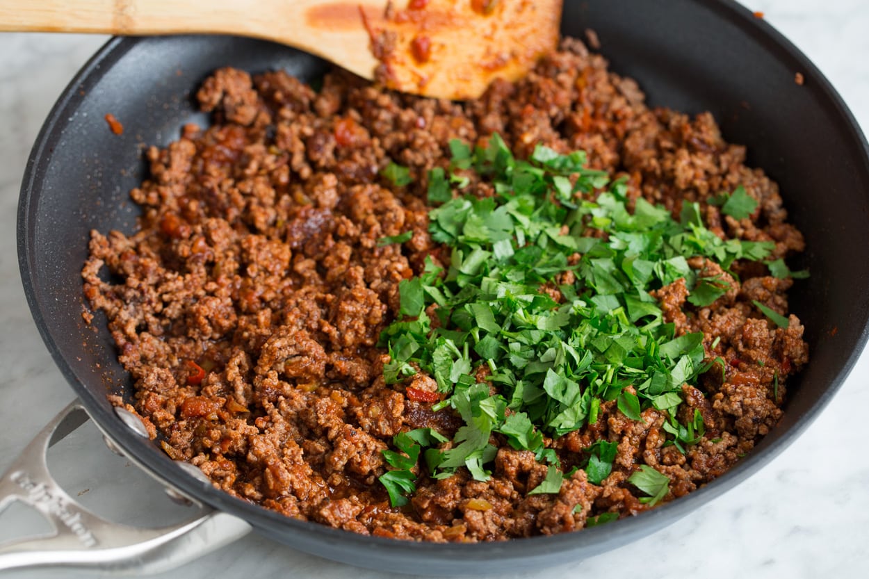 Adding cilantro to finished taco salad beef mixture in skillet.
