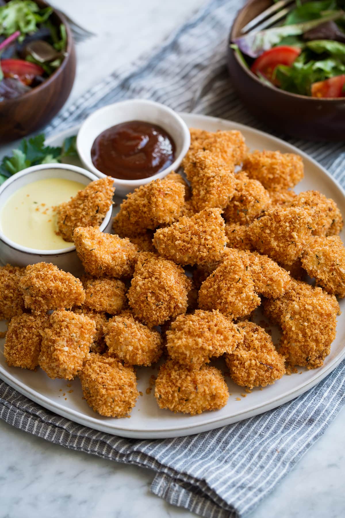 Pile of chicken nuggets on a white serving platter set over a grey napkin on a marble surface.