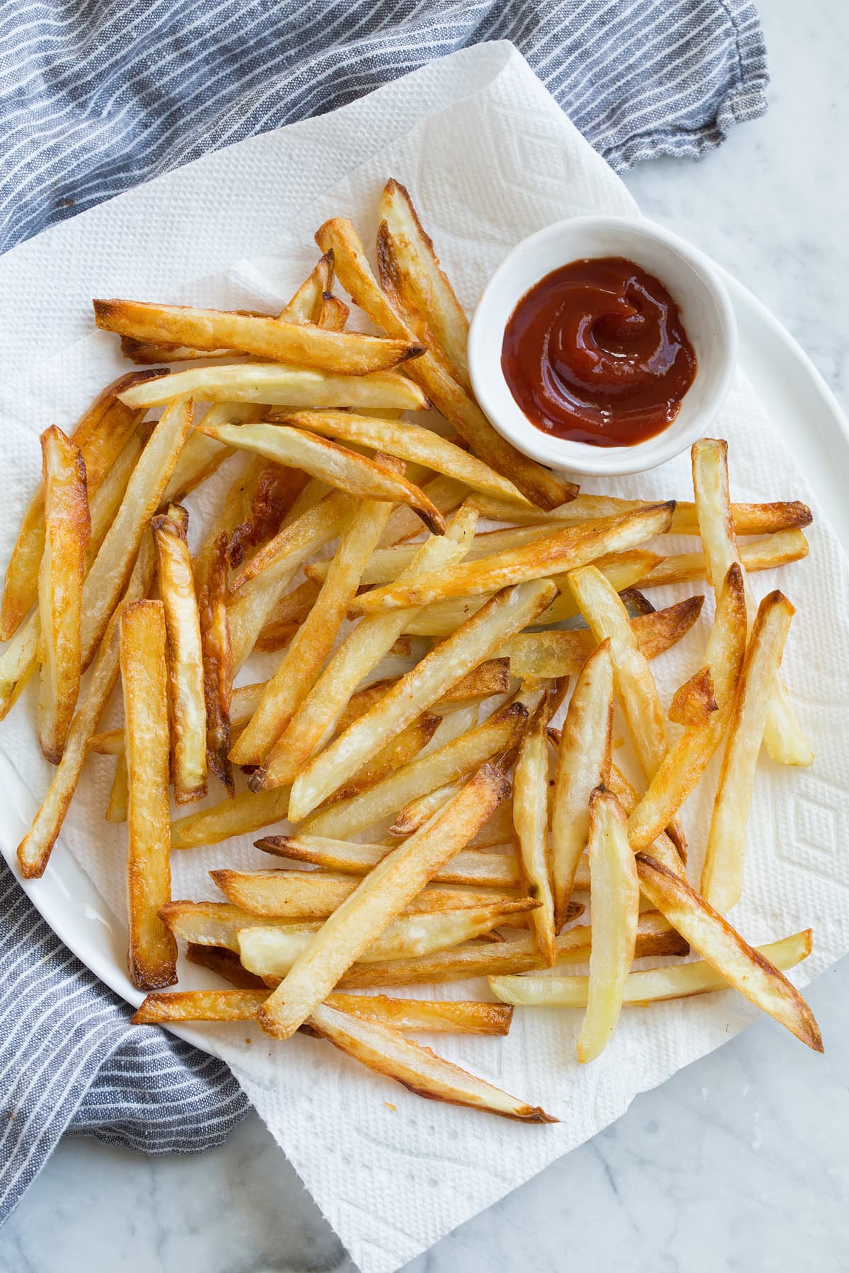 French Fries on a napkin lined plate with a side of ketchup.