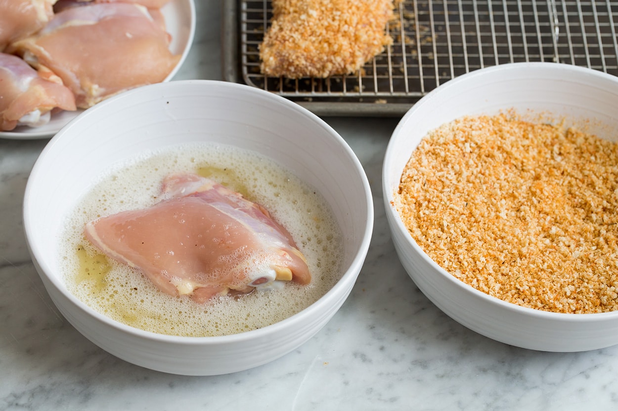 Dressing chicken thigh in egg white in a bowl and panko for Oven Fried Chicken