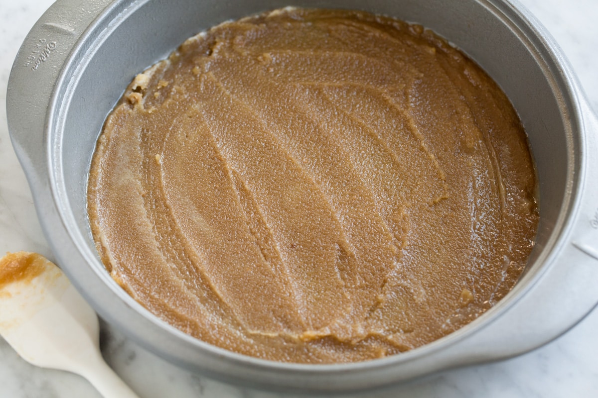 Showing how to make Pineapple Upside Down Cake. Spreading brown sugar butter topping into a 9-inch cake pan.
