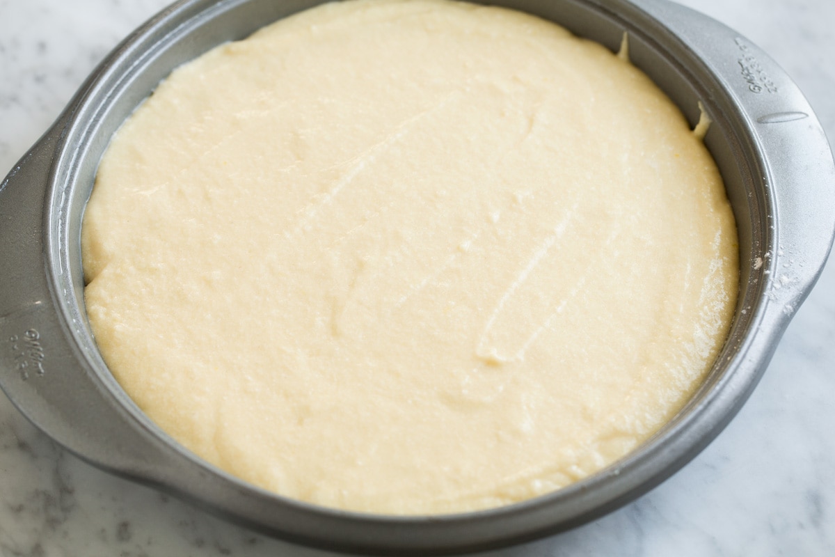 Adding homemade cake batter over pineapple layer in cake pan.