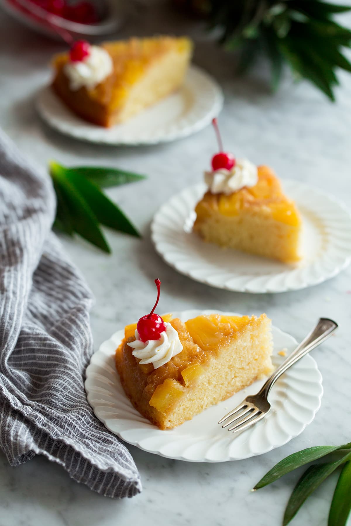 Three slices of Pineapple Upside Down Cake on individual white ruffled dessert plates.