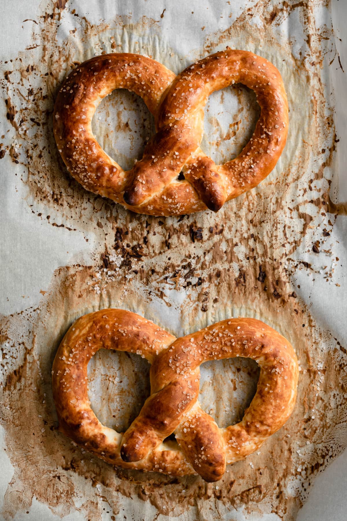 Homemade Soft Pretzels Two pretzels on parchment paper lined baking sheet showing what they should look like after baking with a golden brown color.
