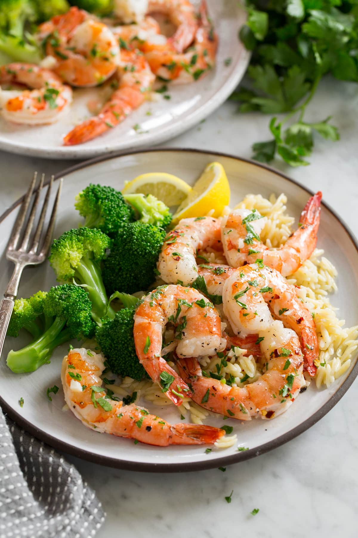 Baked Shrimp with Garlic Lemon Butter Sauce Baked shrimp on a white serving plate with orzo and broccoli.