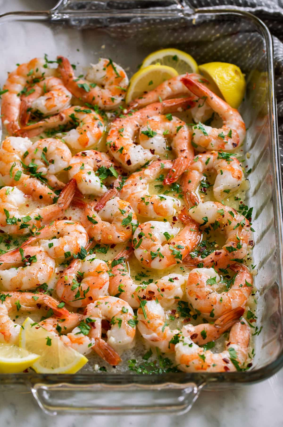 Baked Shrimp with Garlic Lemon Butter Sauce Glass baking dish filled with bake shrimp and garlic butter sauce, garnished with parsley and lemon wedges.