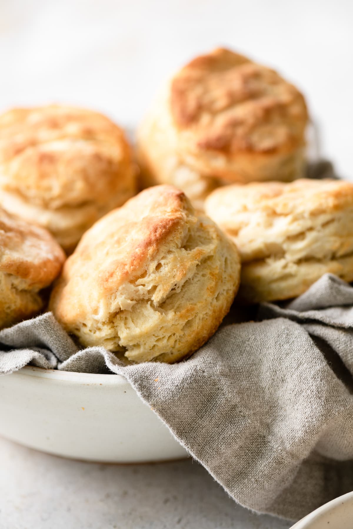 Tall and flaky biscuits stacked in a serving bowl with a grey kitchen cloth.