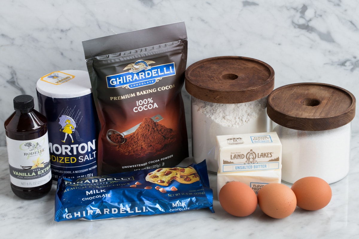 Ingredients needed to make brownies shown here including flour, sugar, eggs, butter, cocoa powder, salt, vanilla and chocolate chips.