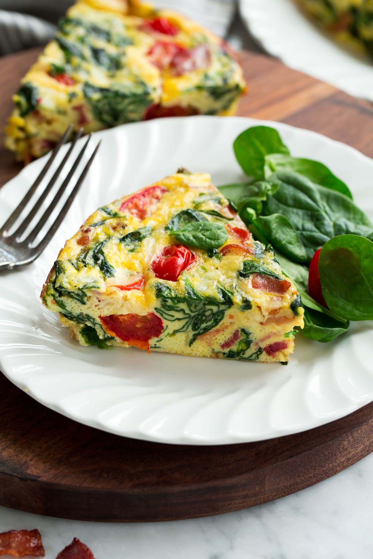 Frittata Recipe (Bacon, Spinach, Tomato and Swiss) Single slice of frittata on a white serving plate.