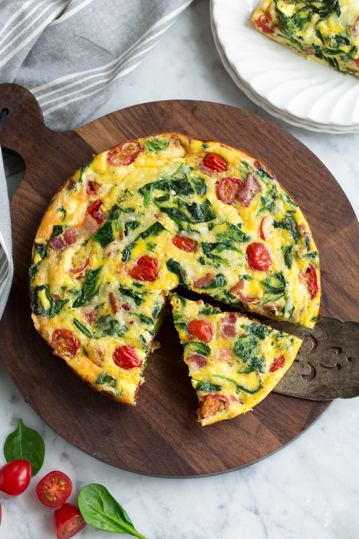 Frittata Recipe (Bacon, Spinach, Tomato and Swiss) Sliced frittata on a wooden surface.