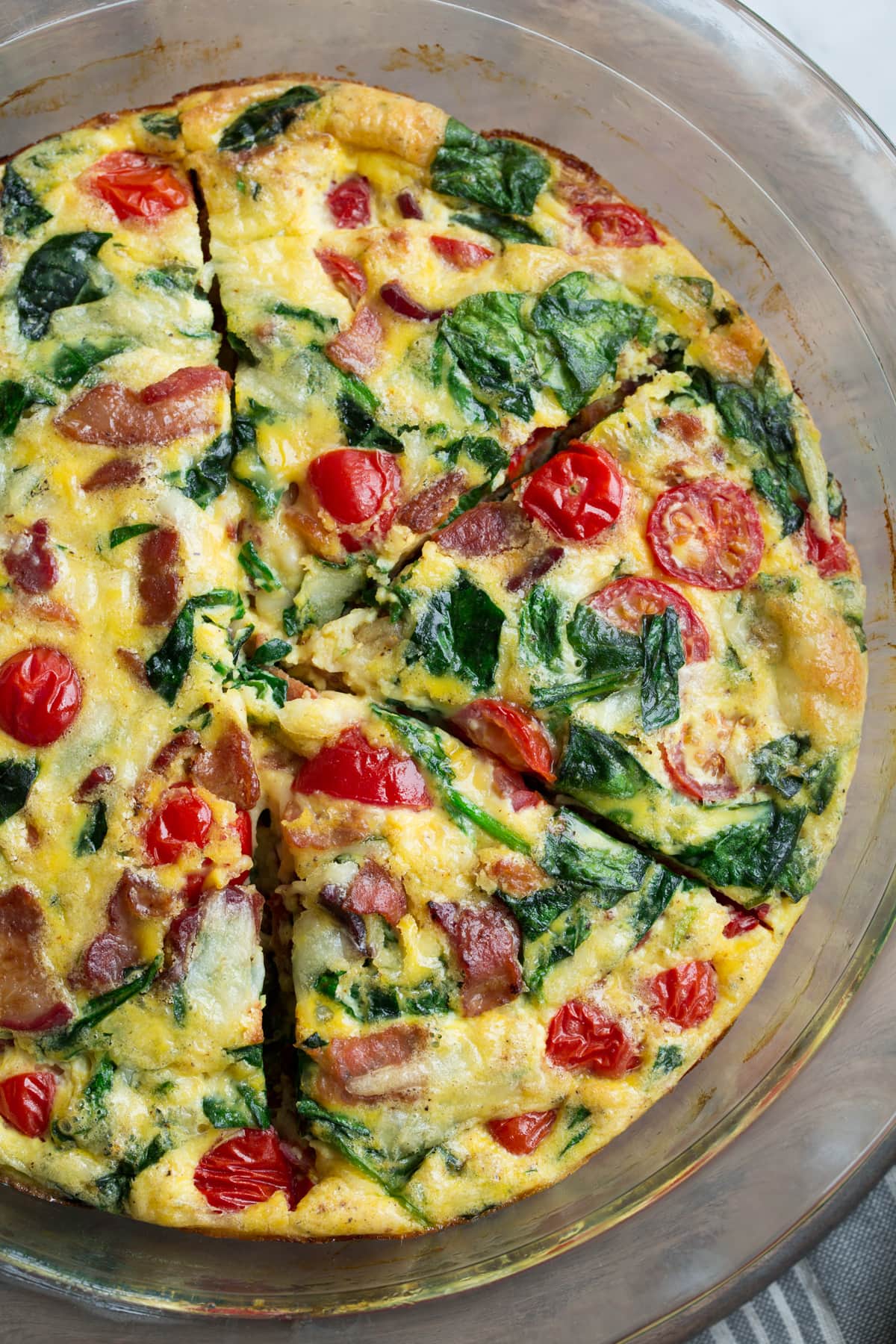 Frittata Recipe (Bacon, Spinach, Tomato and Swiss) Frittata in a glass pie plate set over a wooden surface.