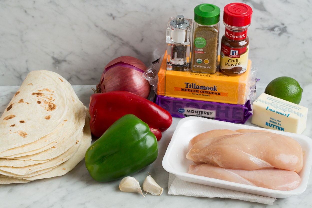 Quesadilla ingredients shown here including tortillas, butter, cheese, chicken, bell peppers, red onion, garlic, cumin, chili powder and lime. 