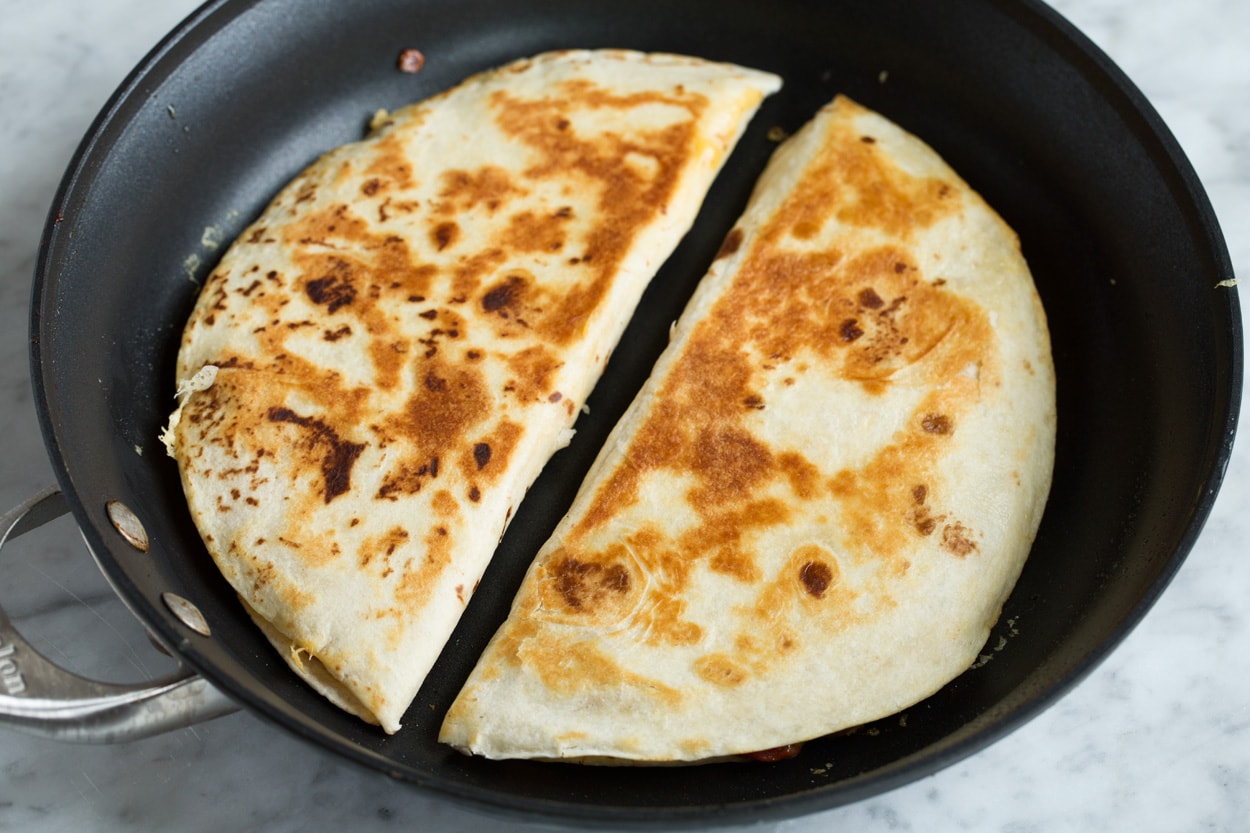 Two quesadillas in a skillet shown after cooking with golden brown exterior.