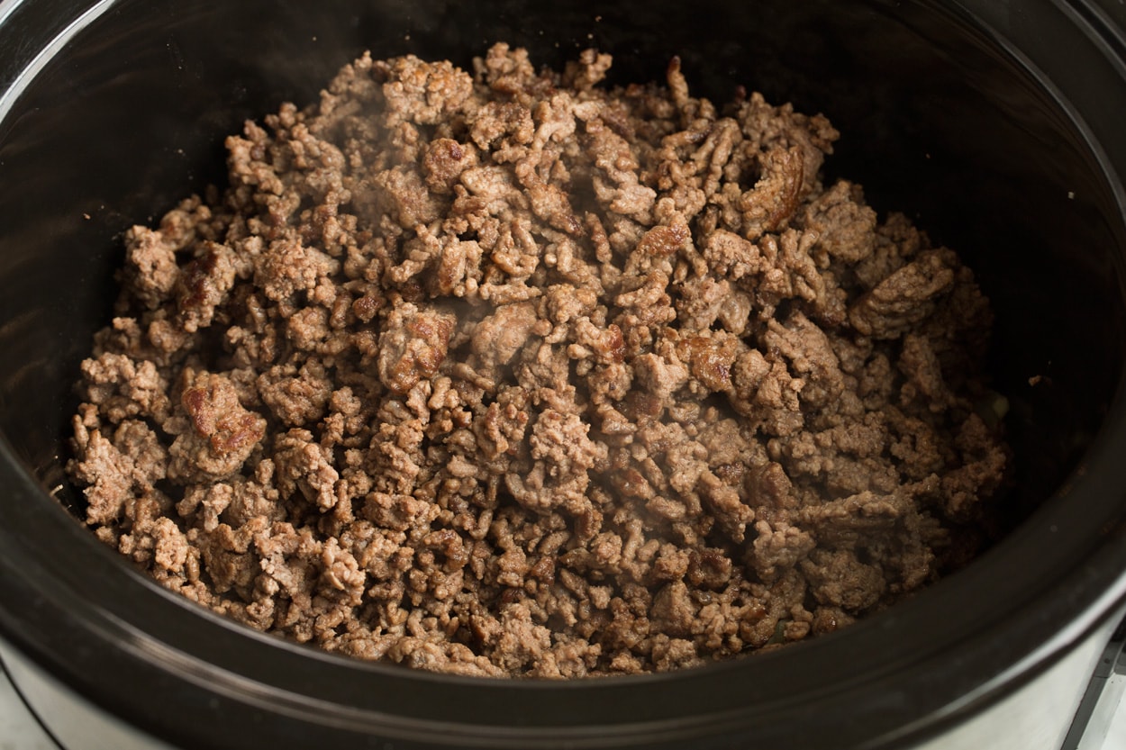 Adding browned beef to slow cooker to make chili.