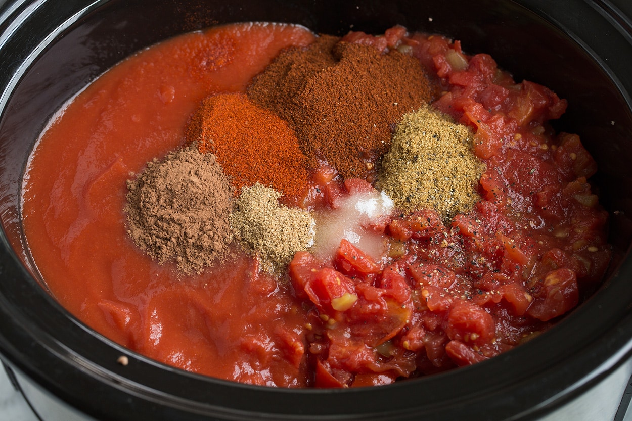 Adding tomatoes, tomato sauce, and spices to slow cooker for chili.