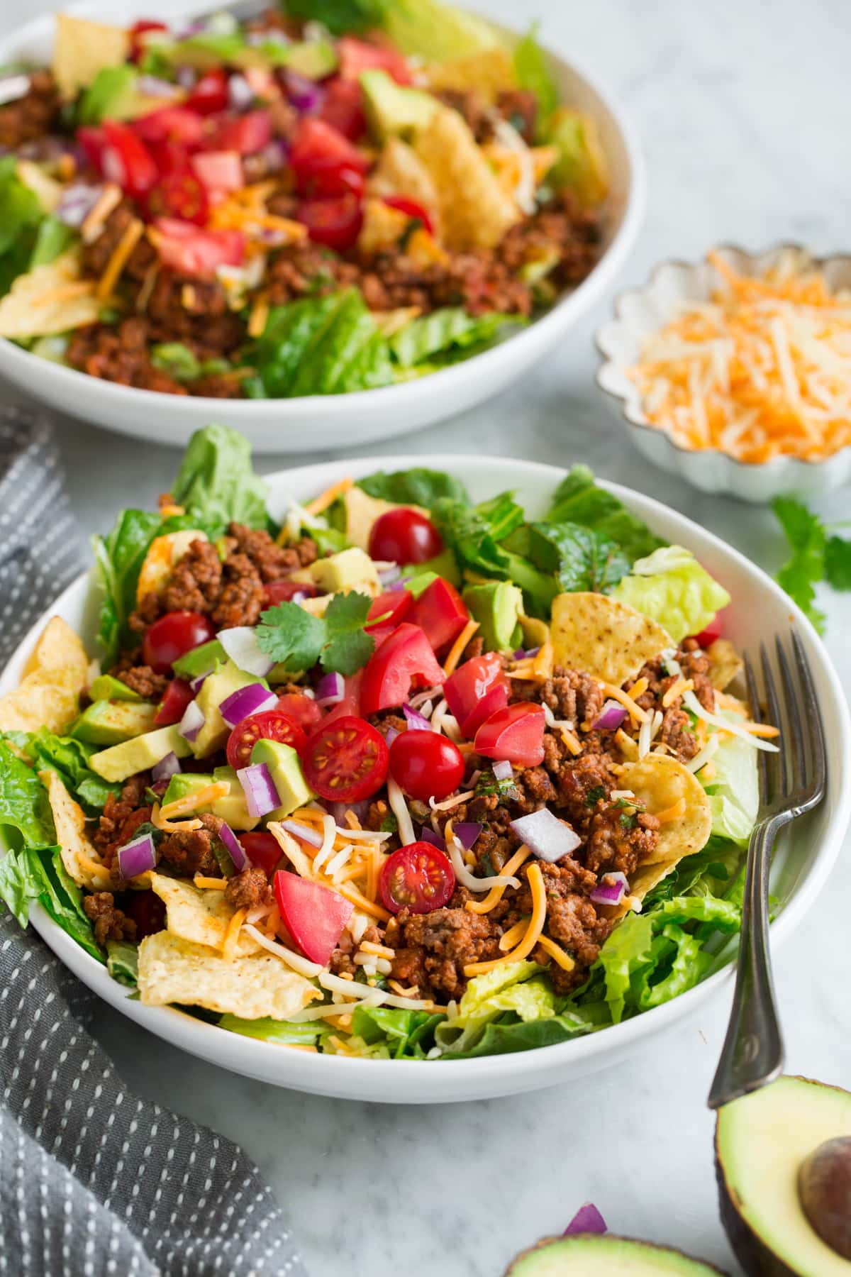 Two servings of taco salad in white bowls set over a marble table.