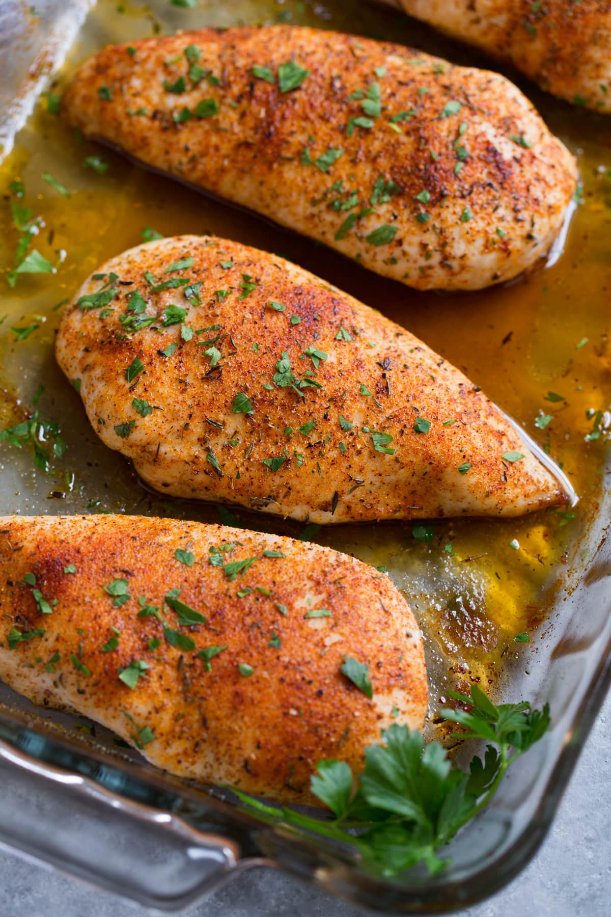 Close up image of chicken breast in glass baking dish set over a grey surface, after baking in the oven.