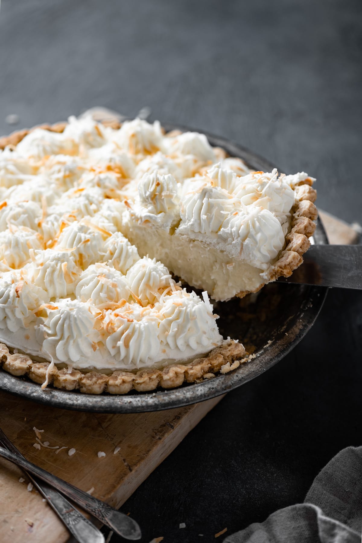 Removing a slice of coconut cream pie from the whole coconut cream pie in pie dish.