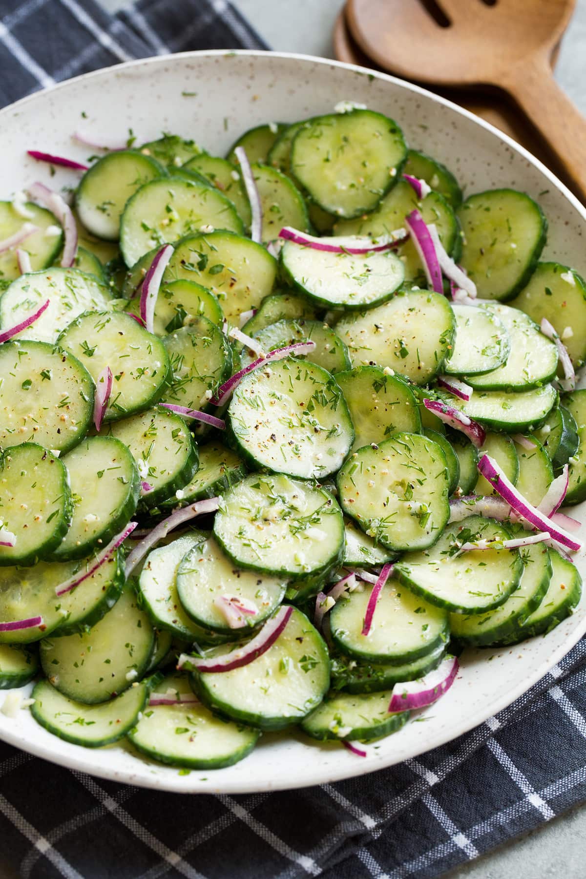 Cucumber salad shown in white ceramic serving bowl set over a dark grey napkin.