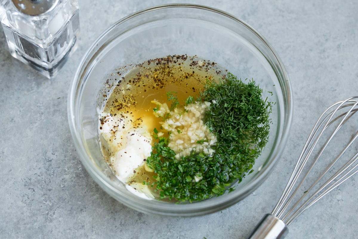 Making cucumber salad dressing. Whisking apple cider vinegar, mayonnaise, honey, olive oil, dill, parsley, garlic, salt and pepper,