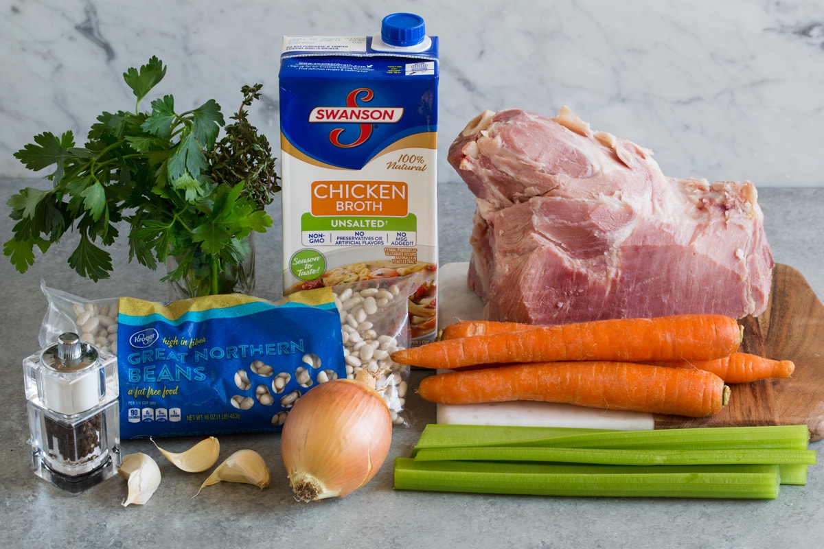 Ham and Bean Soup Ingredients needed for ham and bean soup shown here including meaty ham bone, carrots, celery, onion, garlic, great northern beans, chicken broth, parsley and thyme.
