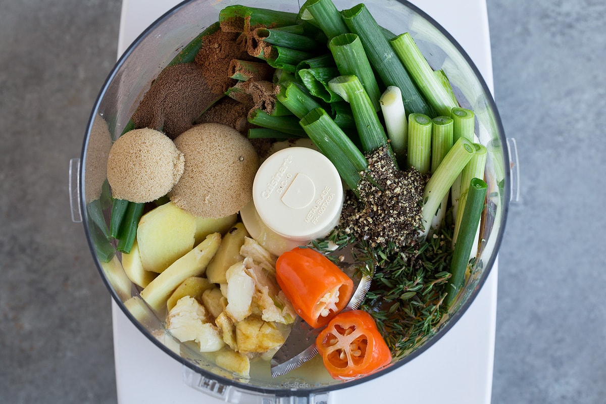 Making jerk chicken marinade. Adding ingredients to food processor including green onions, spices, pepepr, ginger, brown sugar, garlic and thyme.