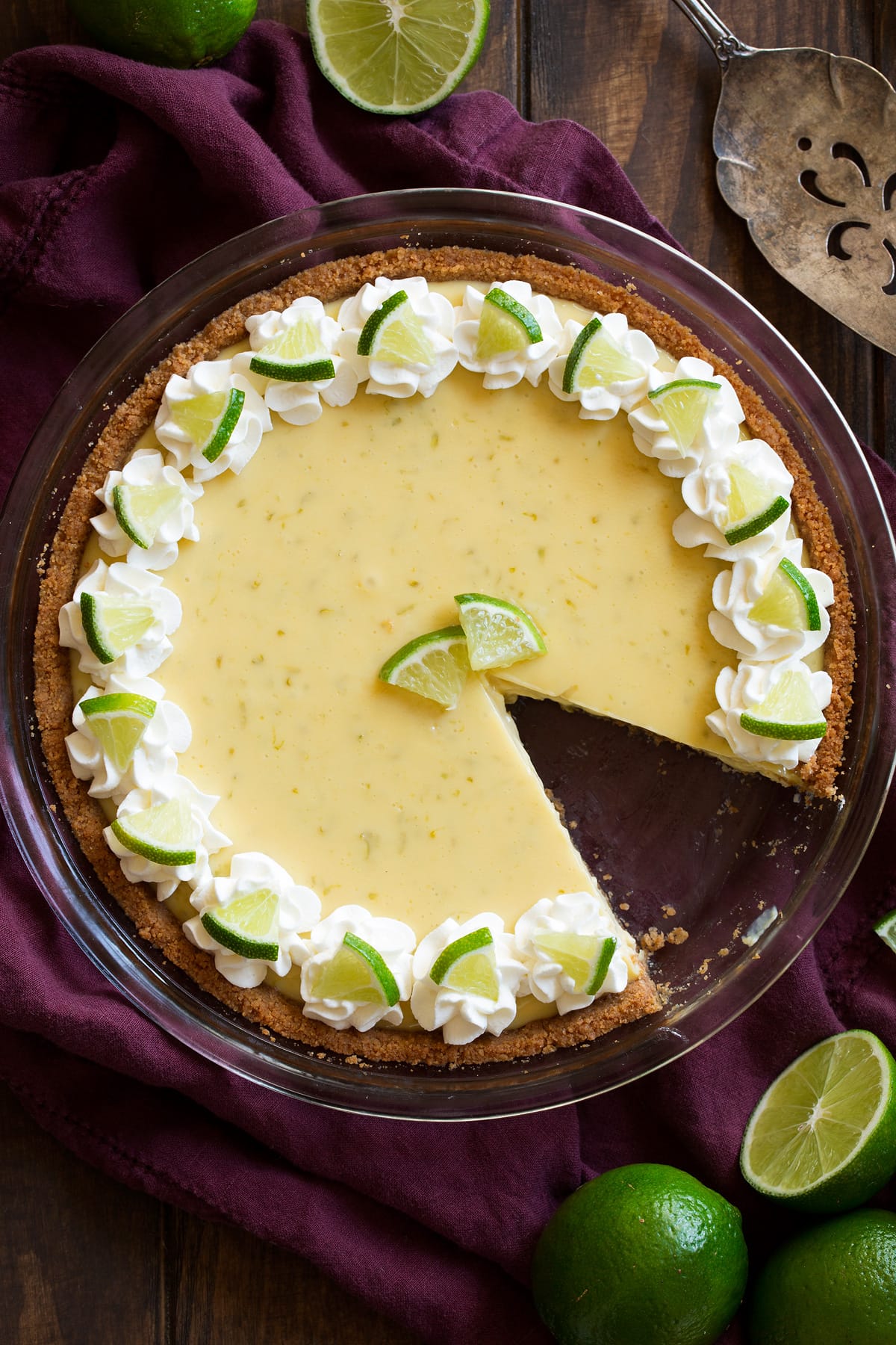 Whole key lime pie with one slice removed. Pie is decorated with swirls of whipped cream around the edges and mini lime slices.
