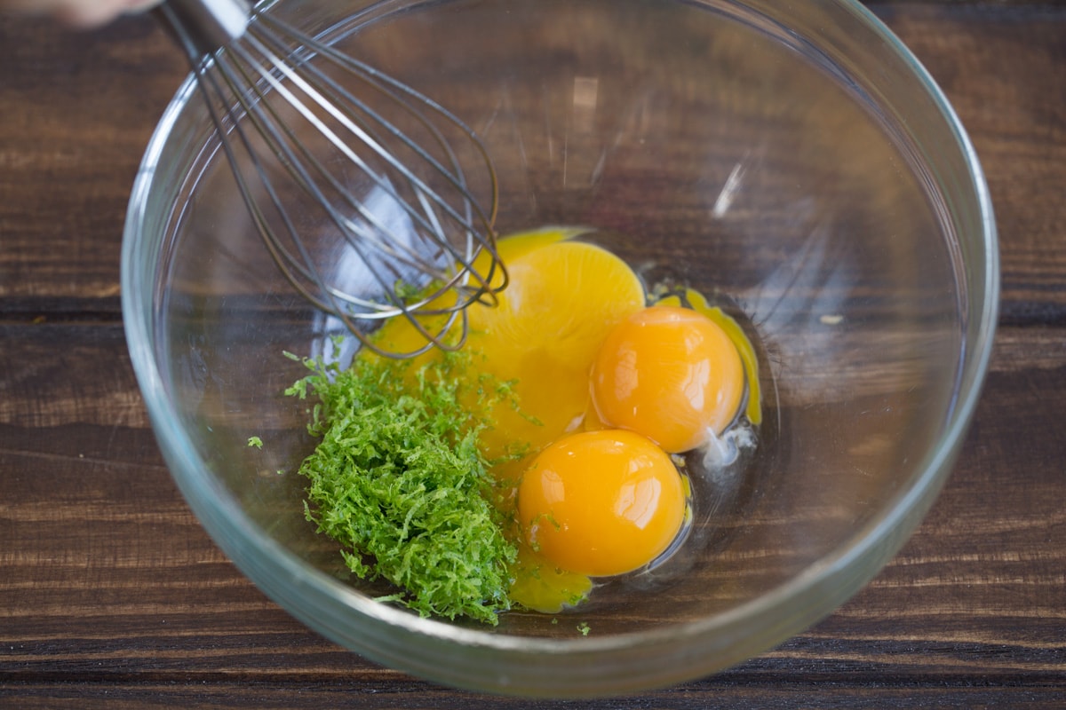 Showing how to make key lime pie filling. Whisking egg yolks and lime zest in a glass mixing bowl.